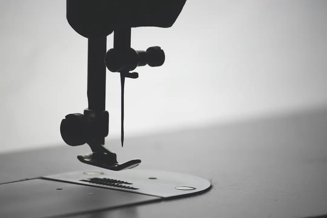 Czarne urządzenie mechaniczne z kołami i zwisającym przewodem unosi się nad białą, zaokrągloną platformą, rzucając cienie w surowej, minimalistycznej scenerii.